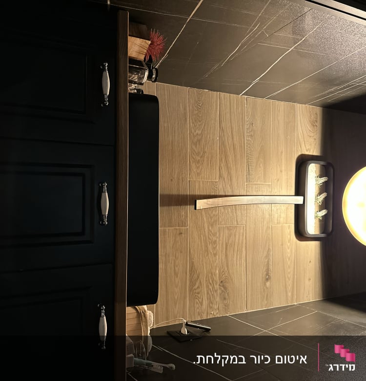 ארון שחור עם ידיות לבנות, רצפת עץ, מנורה עגולה